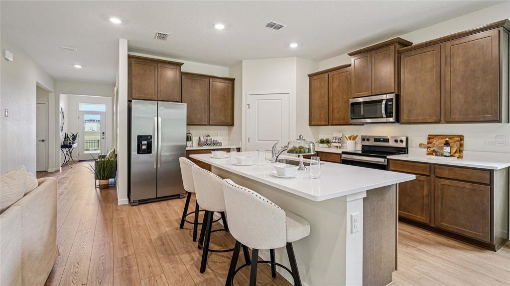 A kitchen features dark wood cabinets, a white quartz island with bar seating, and stainless appliances — 3018 CANOPY OAK BOULEVARD, WILDWOOD, FL