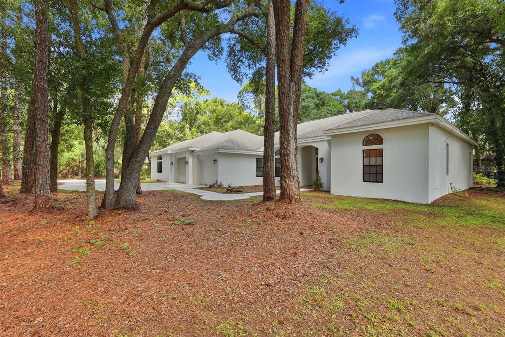 A white single-story house with a multi-car garage sits among trees on a wooded lot — 6301 S 86TH AVENUE N, PINELLAS PARK, FL