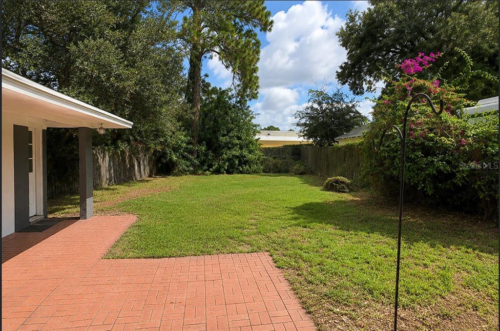 A backyard features a red brick patio, a grassy lawn, and a wooden privacy fence — 310 GRANADA DRIVE, WINTER PARK, FL