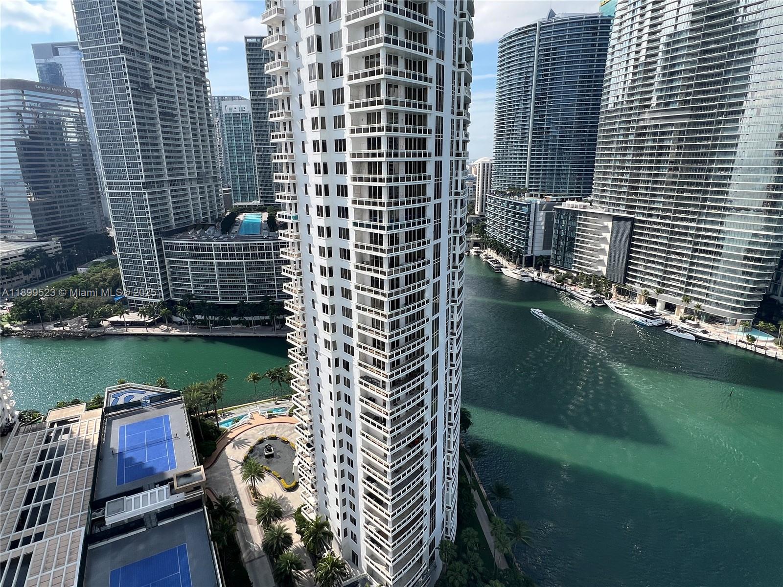 An aerial view shows a tall residential tower surrounded by high-rise buildings and a canal — 900 Brickell Key Blvd # 2205, Miami FL 33131, MIAMI, FL