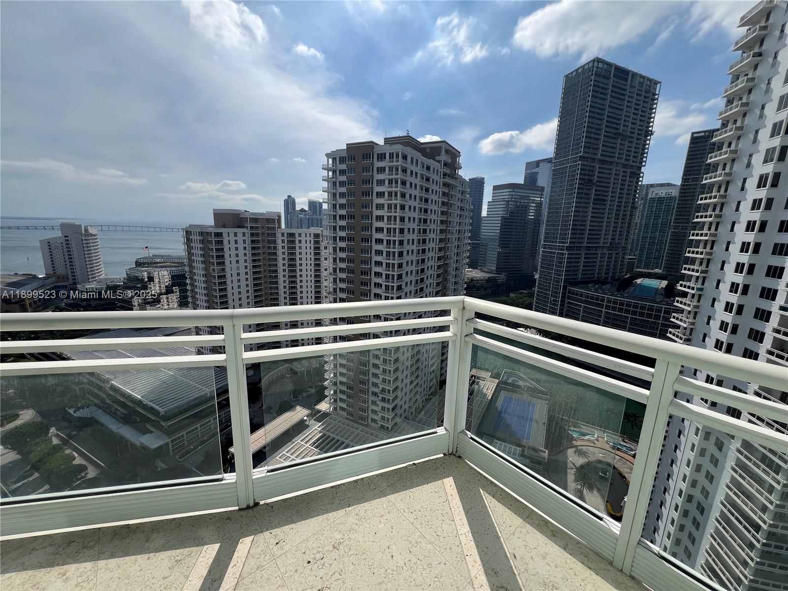 A high-rise balcony overlooks a dense urban cityscape with multiple skyscrapers and a distant bay — 900 Brickell Key Blvd # 2205, Miami FL 33131, MIAMI, FL
