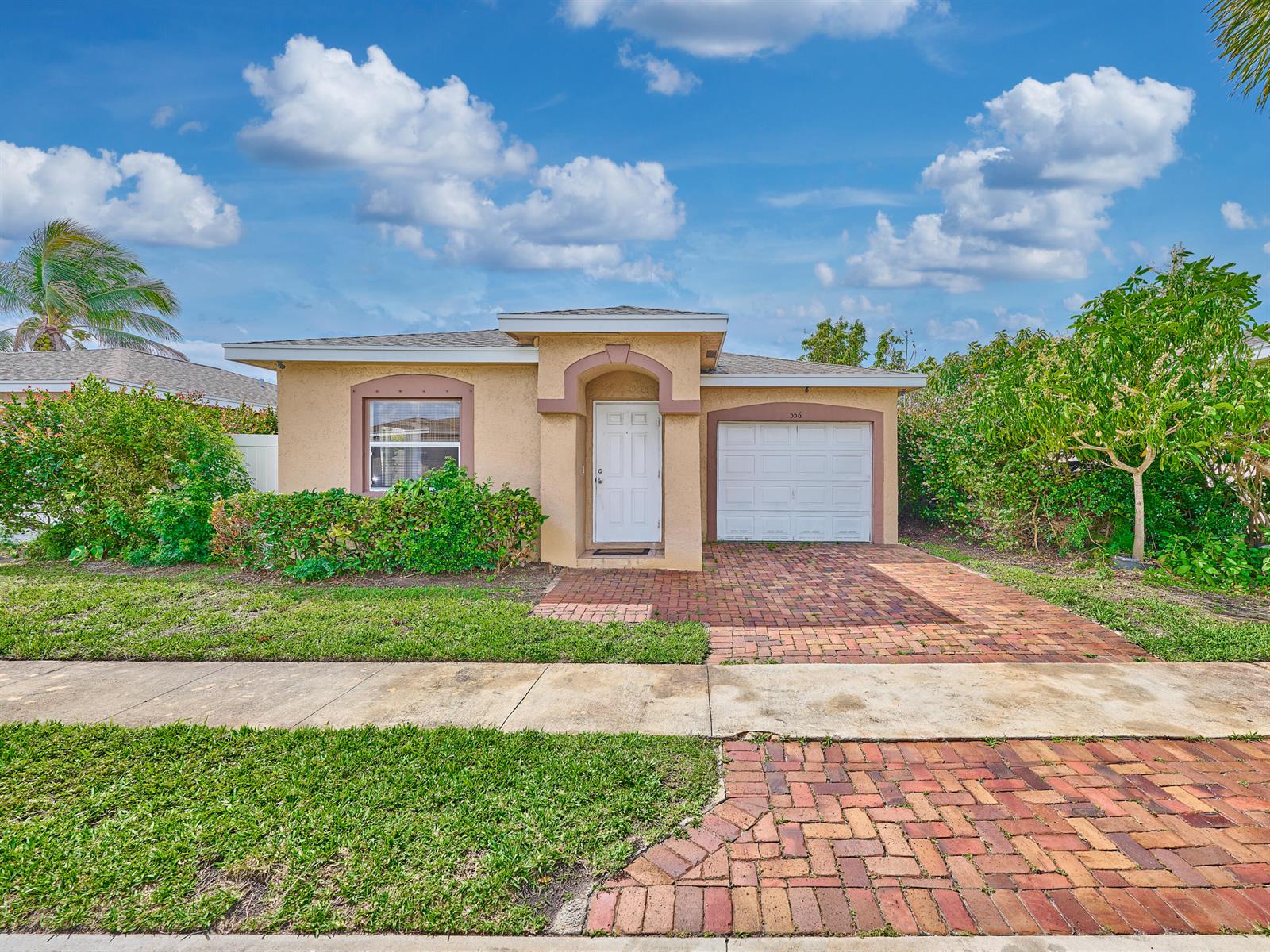 A single-story house with a tan stucco exterior, a brick driveway, and a white garage door — 556 E Ridge Cir Circle N, Boynton Beach FL 33435, BOYNTON BEACH, FL