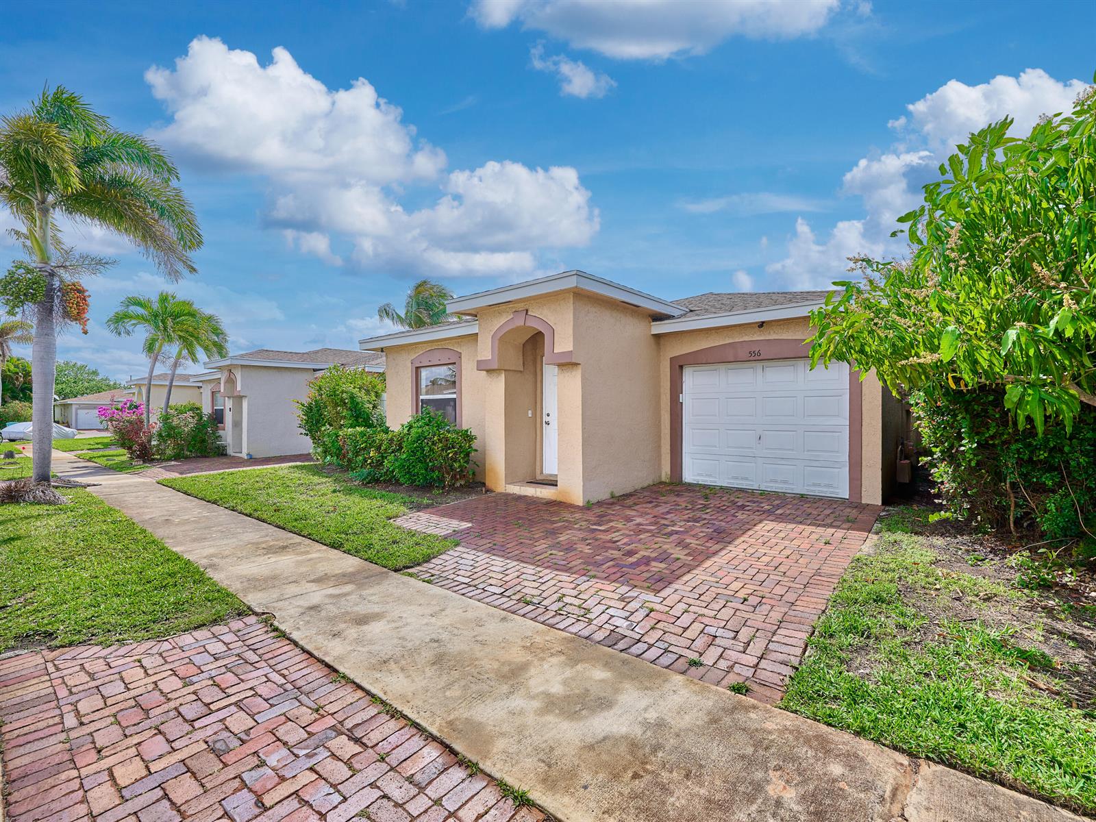 A single-story house with a brick driveway, white garage door, and palm trees — 556 E Ridge Cir Circle N, Boynton Beach FL 33435, BOYNTON BEACH, FL