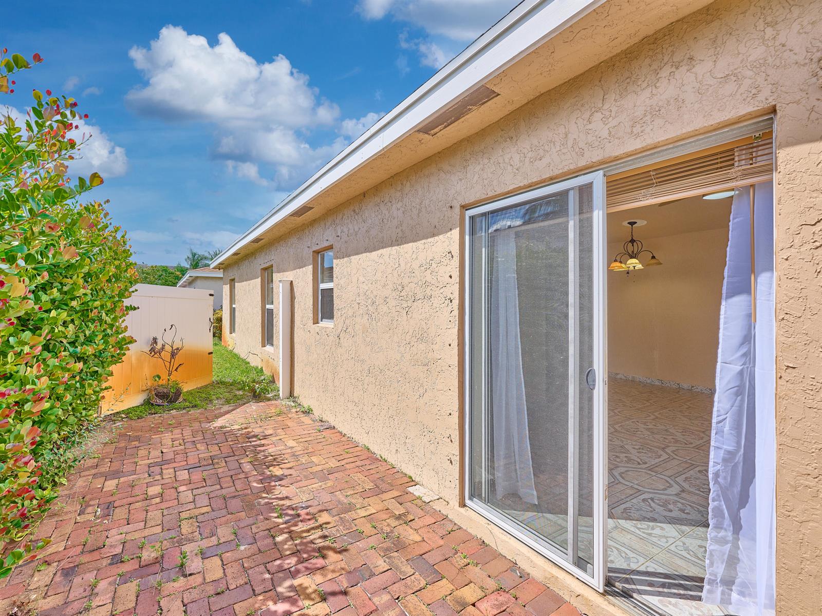 A brick patio sits outside a house with a sliding glass door and stucco walls — 556 E Ridge Cir Circle N, Boynton Beach FL 33435, BOYNTON BEACH, FL