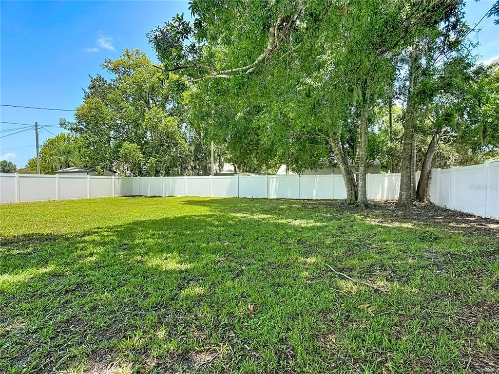 A grassy backyard features a white vinyl fence and several large shade trees — 517 ILLINOIS AVENUE, ST CLOUD, FL