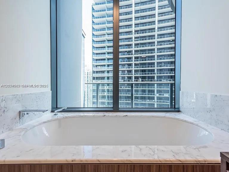 A white soaking tub is set into a marble-topped deck before a large window — 1000 Brickell Plz # 3509, Miami FL 33131, MIAMI, FL