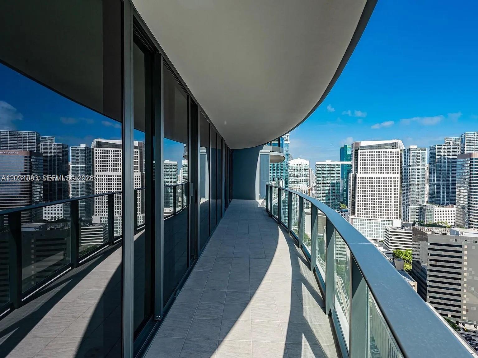 A curved balcony with glass railings overlooks a dense city skyline under a clear sky — 1000 Brickell Plz # 3509, Miami FL 33131, MIAMI, FL