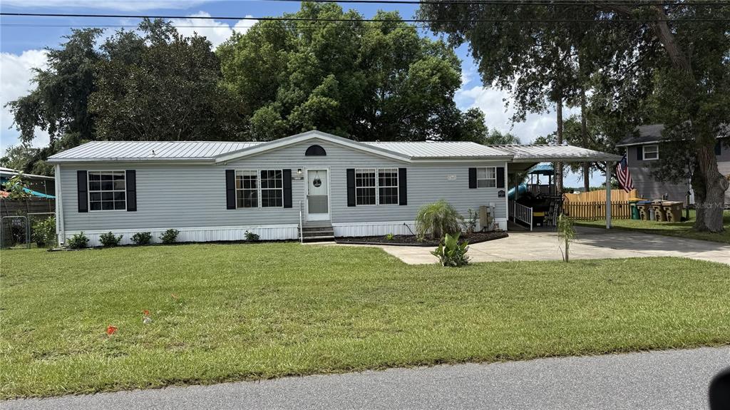 A single-story light gray mobile home with a metal roof and an attached carport — 6344 BASS HIGHWAY, ST CLOUD, FL