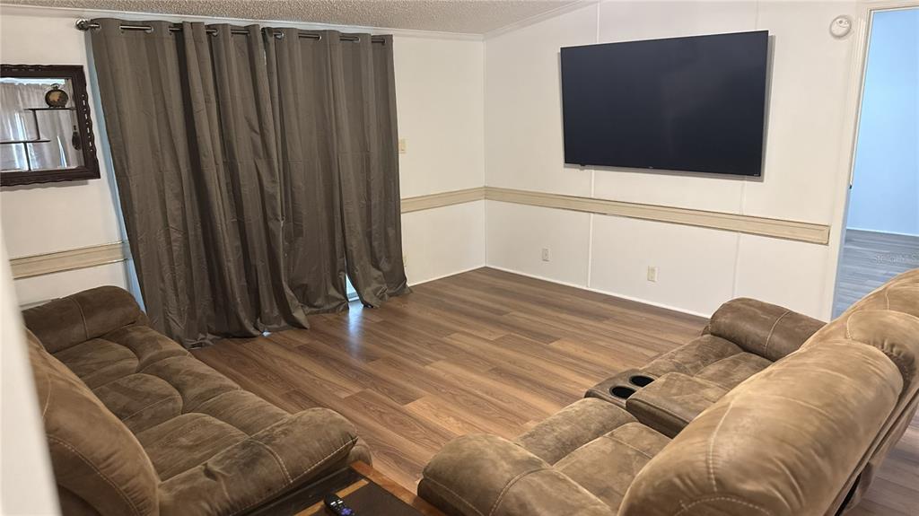 A living room features wood-look flooring, brown sofas, a wall-mounted television, and floor-length curtains — 6344 BASS HIGHWAY, ST CLOUD, FL