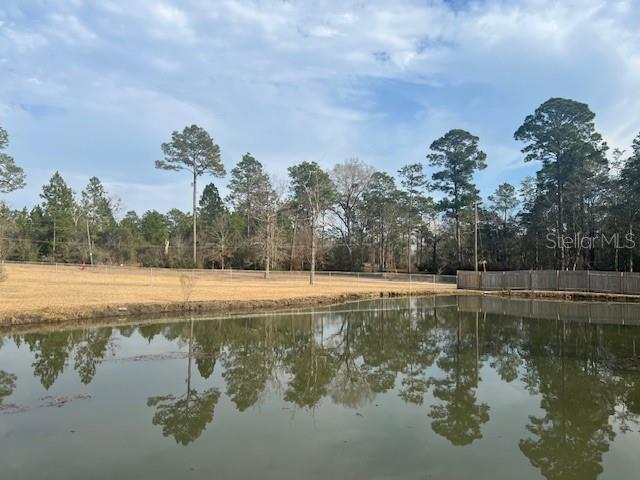 A calm pond reflects the surrounding trees and a fenced grassy yard under a cloudy sky — 1347 WISHBONE ROAD, CANTONMENT, FL