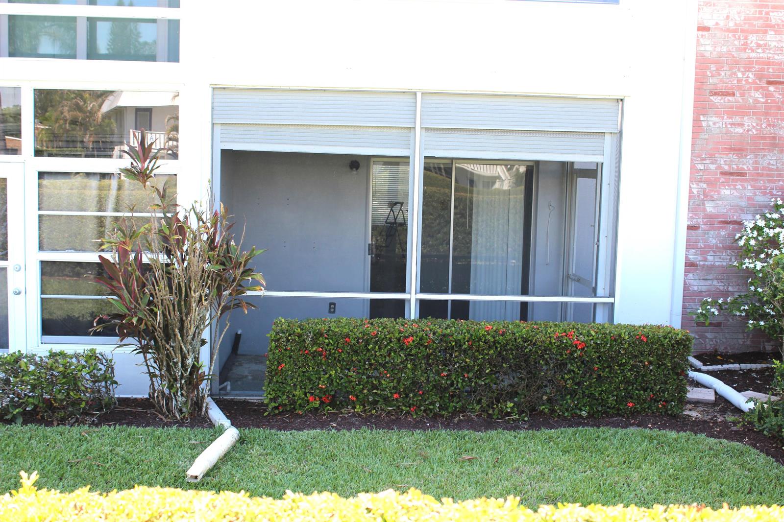 A ground-level patio with a screen enclosure and roll-down shutters sits beside a brick wall — 2929 SE Ocean Boulevard # 2, Stuart FL 34996, STUART, FL