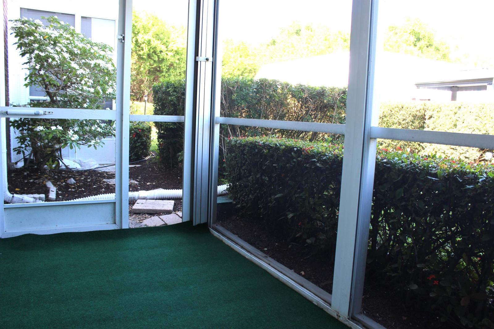 A screened-in porch with green outdoor carpeting looks out onto a hedge and garden — 2929 SE Ocean Boulevard # 2, Stuart FL 34996, STUART, FL