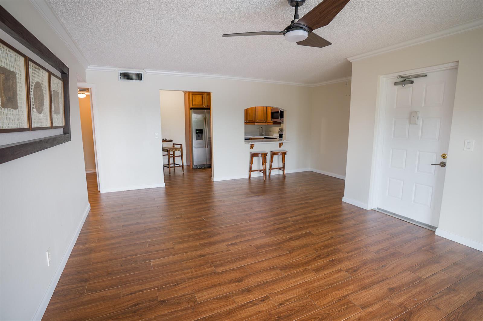 An open living area features wood-look flooring, a ceiling fan, and a kitchen pass-through window — 707 Sunny Pine Way # C2, FL 33415, FL