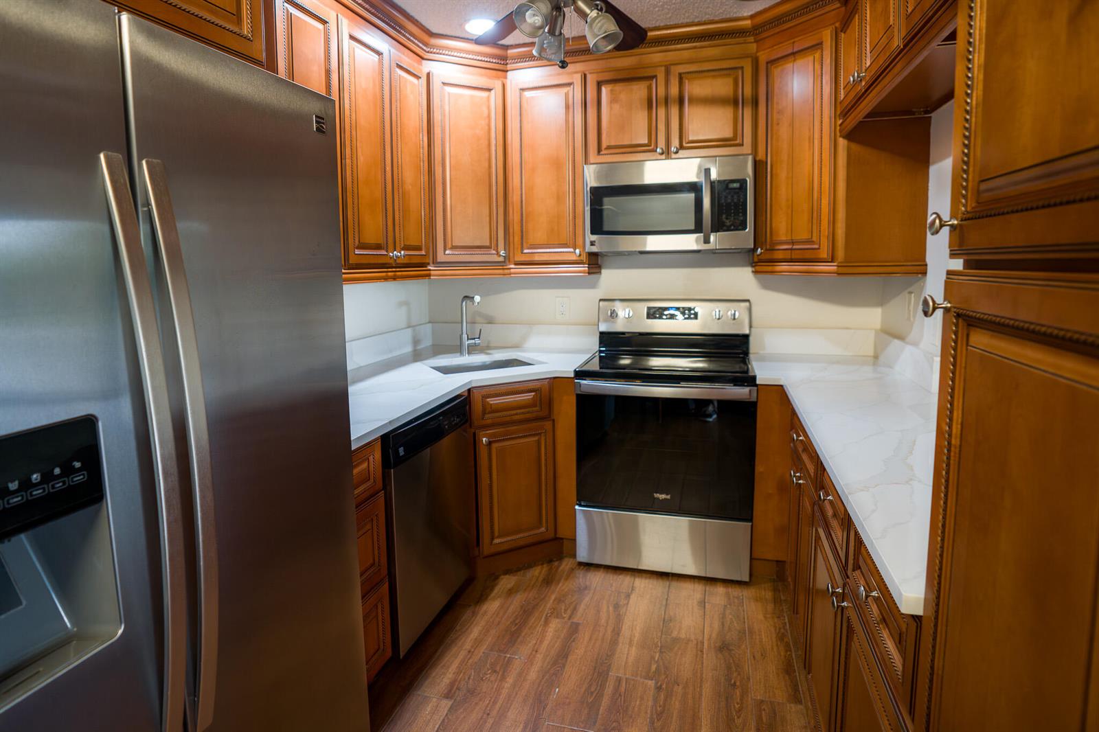 A kitchen features stainless steel appliances, wood cabinets, and white countertops with a corner sink — 707 Sunny Pine Way # C2, FL 33415, FL