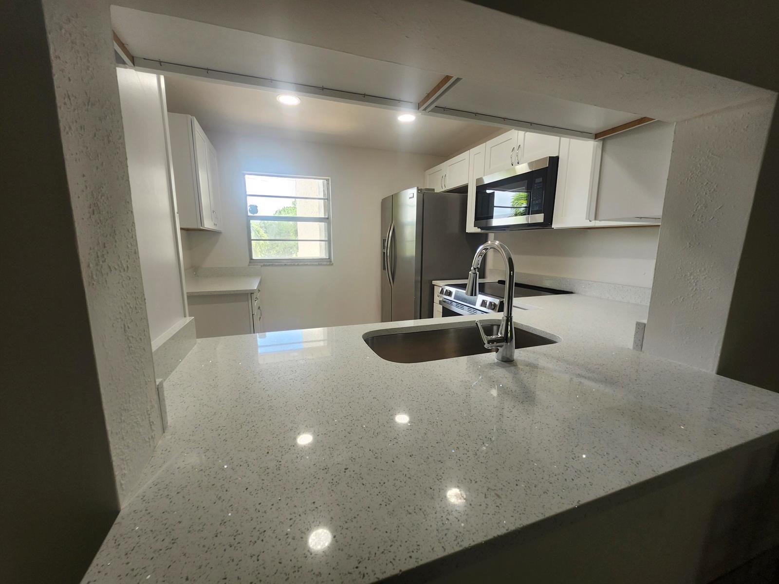 A kitchen features white cabinets, stainless steel appliances, and a speckled quartz countertop with sink — 330 NE 26th Avenue # 202, Boynton Beach FL 33435, BOYNTON BEACH, FL