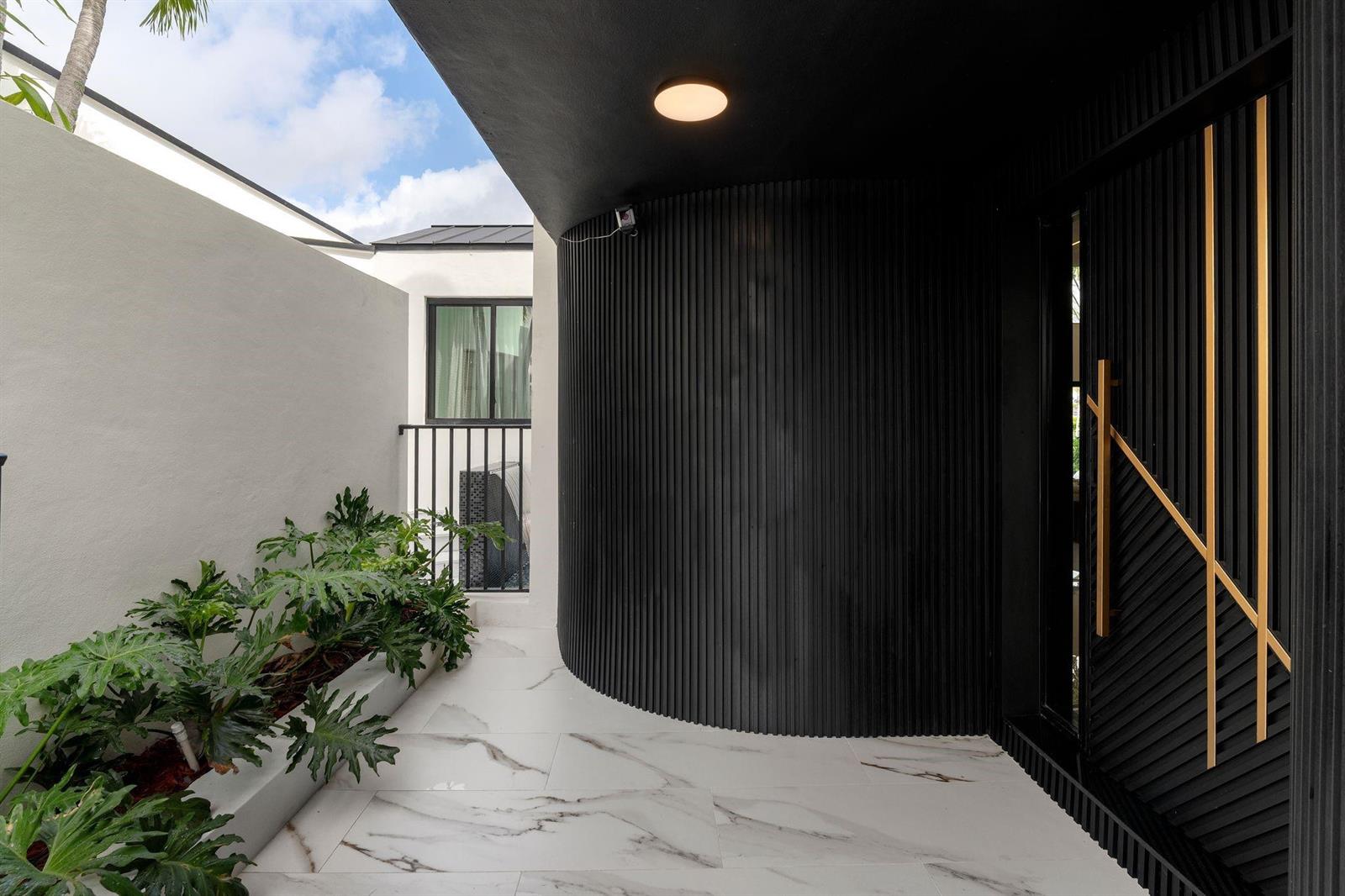 A curved black slatted wall stands beside a modern door on a marble-tiled patio — 2651 NE 22nd Court, Pompano Beach FL 33062, POMPANO BEACH, FL