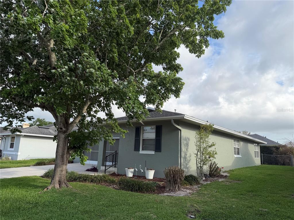 A single-story house with a green exterior, dark shutters, and a large tree in front — 1454 GRAND CAYMAN CIRCLE, WINTER HAVEN, FL