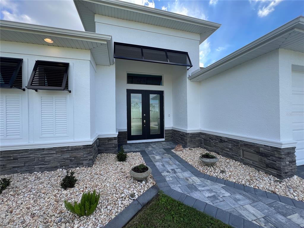 The front exterior of a white house features a stone base and double glass doors — 15419 APPLETON BOULEVARD, PORT CHARLOTTE, FL