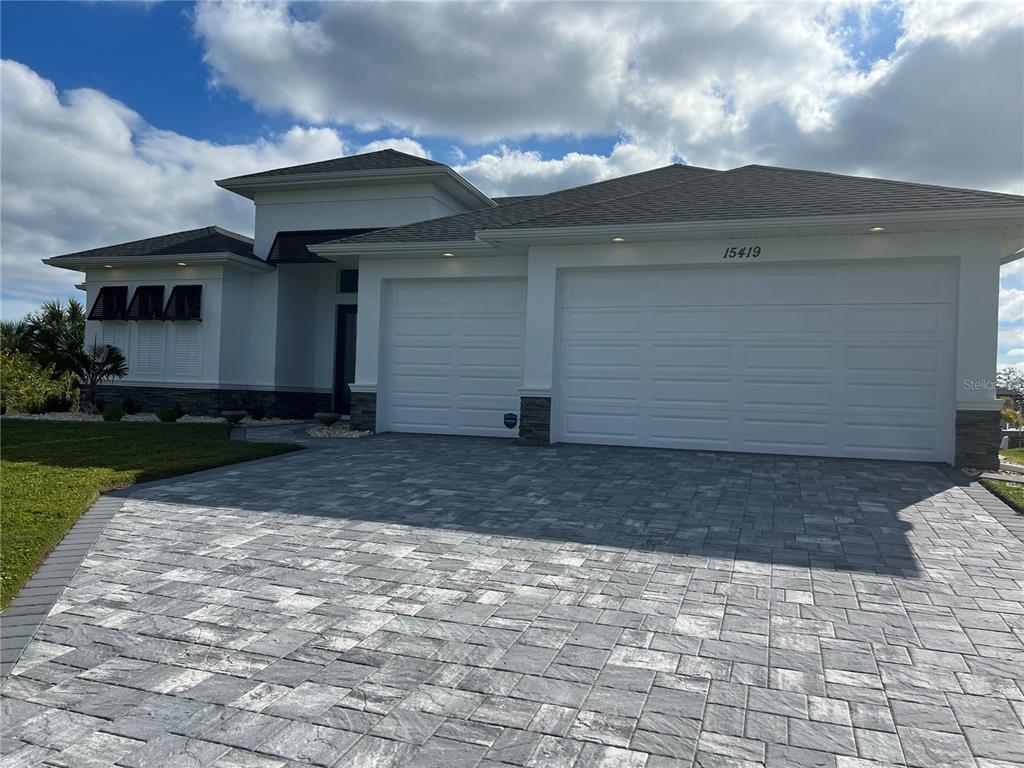 A modern single-story house with a white exterior, stone accents, and a gray paver driveway — 15419 APPLETON BOULEVARD, PORT CHARLOTTE, FL
