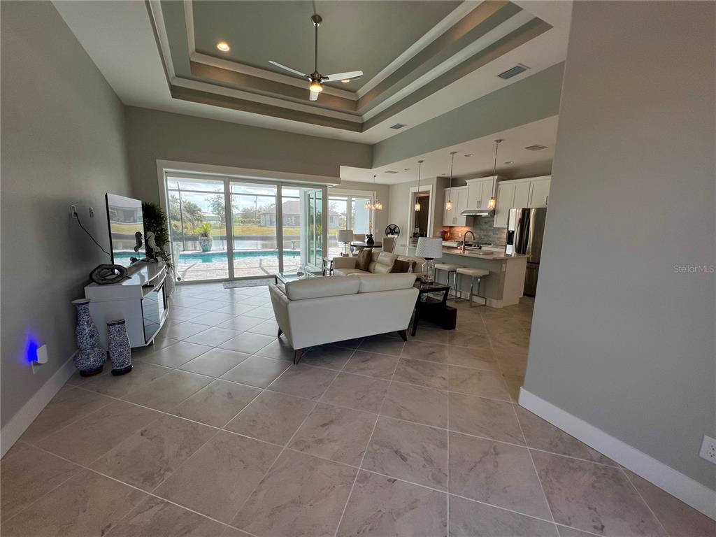 An open-concept living room and kitchen feature tile flooring, a tray ceiling, and pool views — 15419 APPLETON BOULEVARD, PORT CHARLOTTE, FL