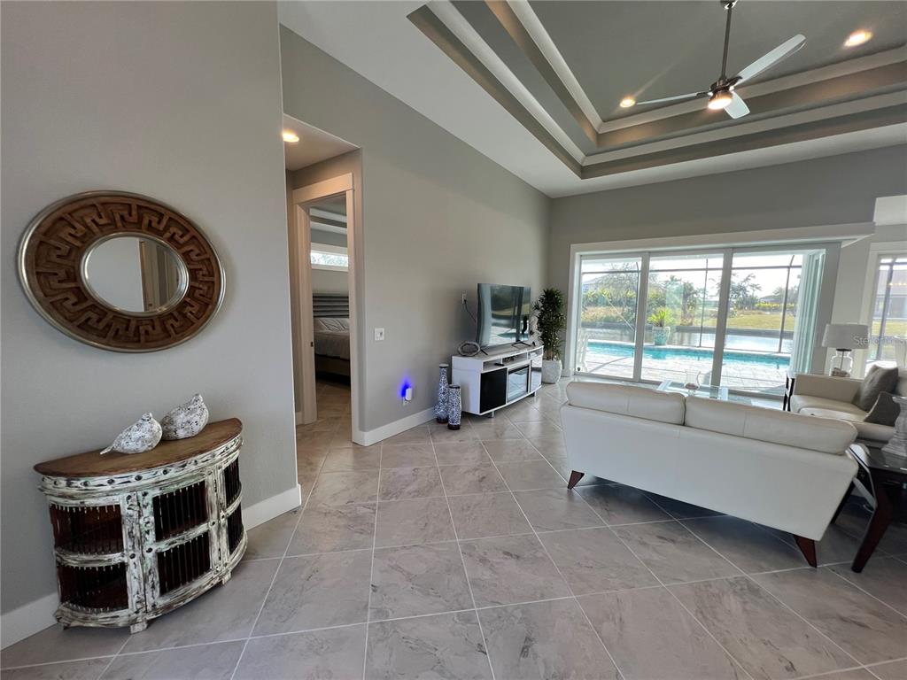 A living room with tile floors, a tray ceiling, and a view of a pool — 15419 APPLETON BOULEVARD, PORT CHARLOTTE, FL