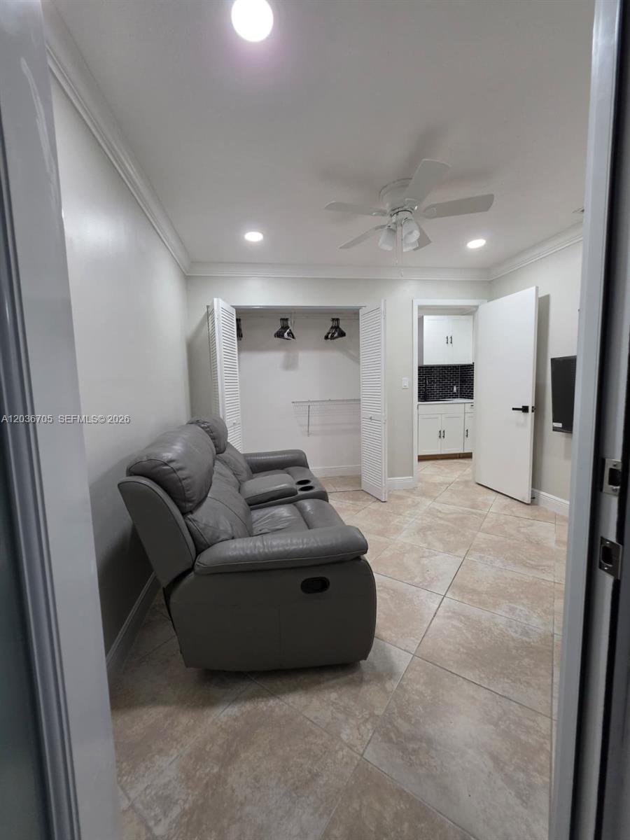 A room with light-colored tile flooring, a gray reclining sofa, a closet, and a kitchenette — MIAMI, FL