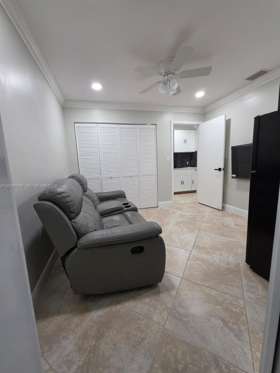 A room with a gray reclining sofa, tile flooring, and a view into a kitchen — MIAMI, FL