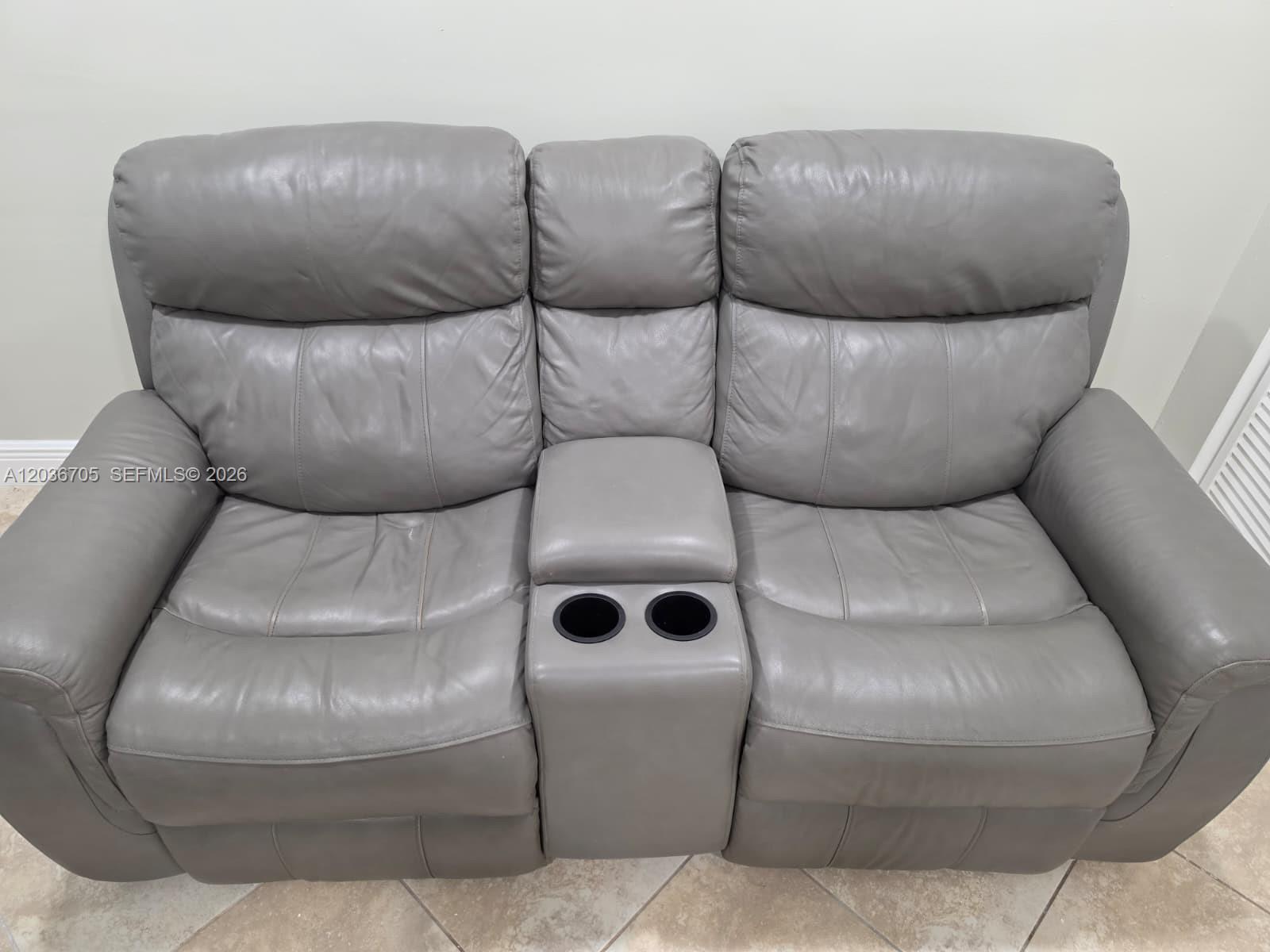 A gray leather loveseat with a center console and two cup holders sits on tile — MIAMI, FL