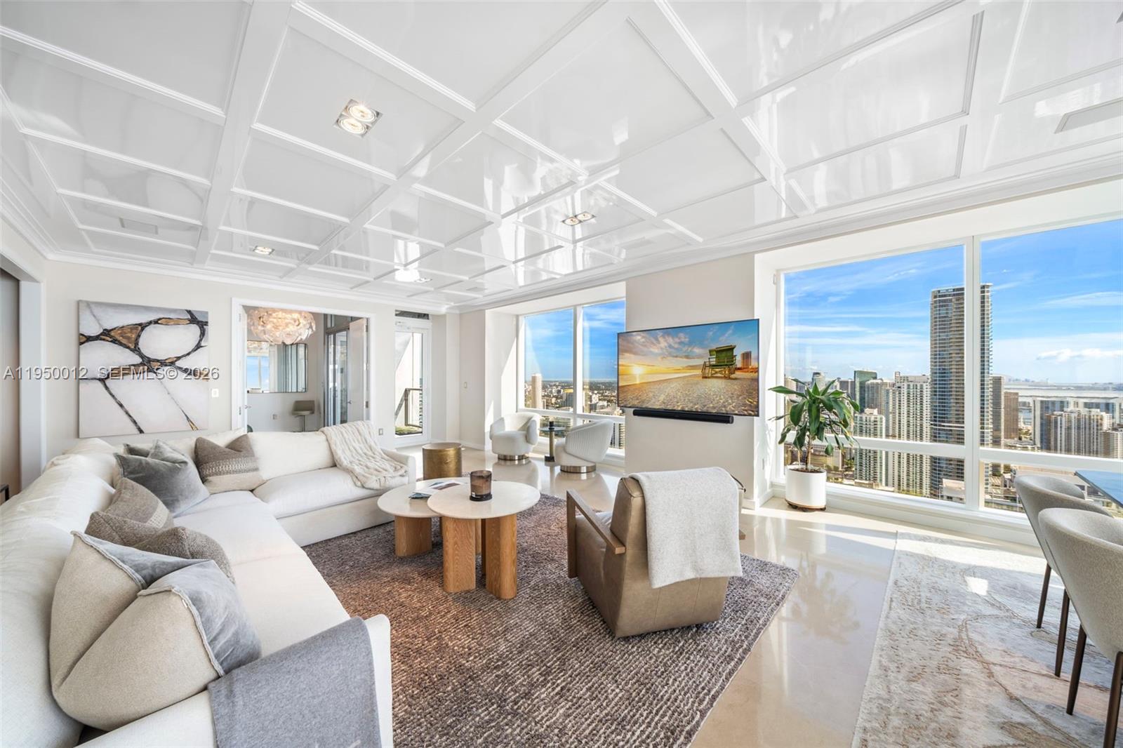 A modern living room features a coffered ceiling, white sofa, and floor-to-ceiling city views — 1425 Brickell Ave # 58E, Miami FL 33131, MIAMI, FL