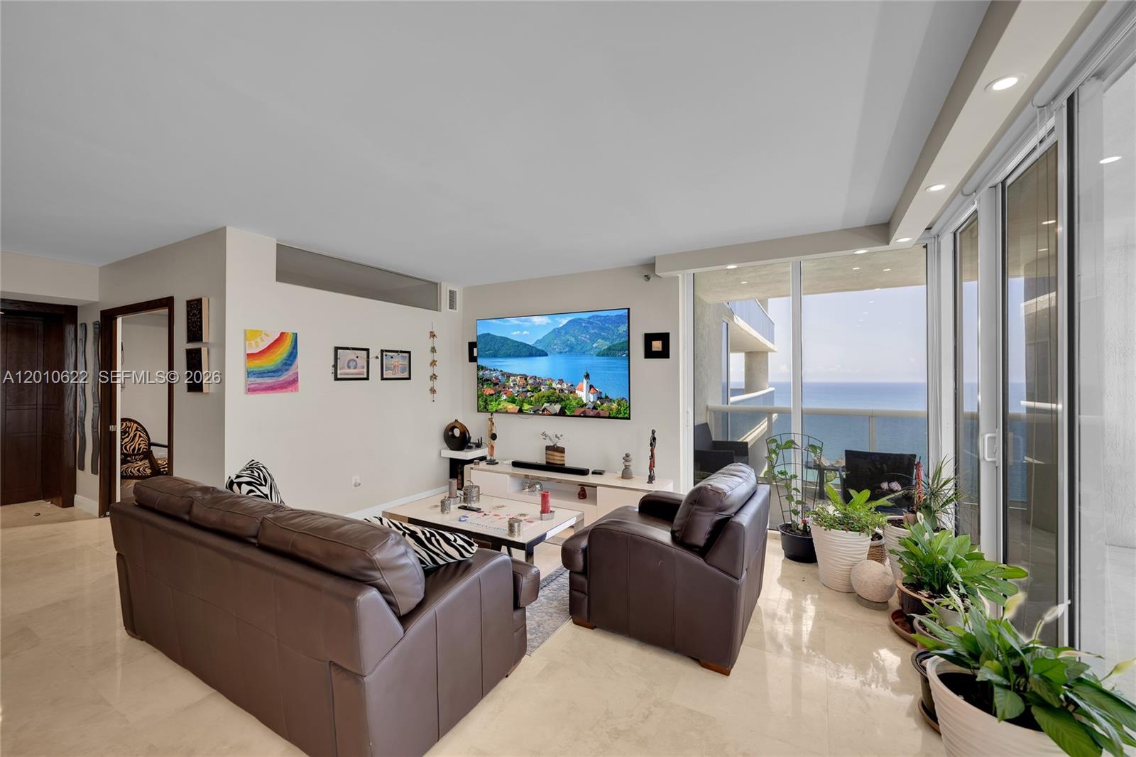 A living room features leather furniture, a wall-mounted television, and floor-to-ceiling windows overlooking the ocean — 1800 S Ocean Dr # 2205, Hallandale Beach FL 33009, HALLANDALE BEACH, FL