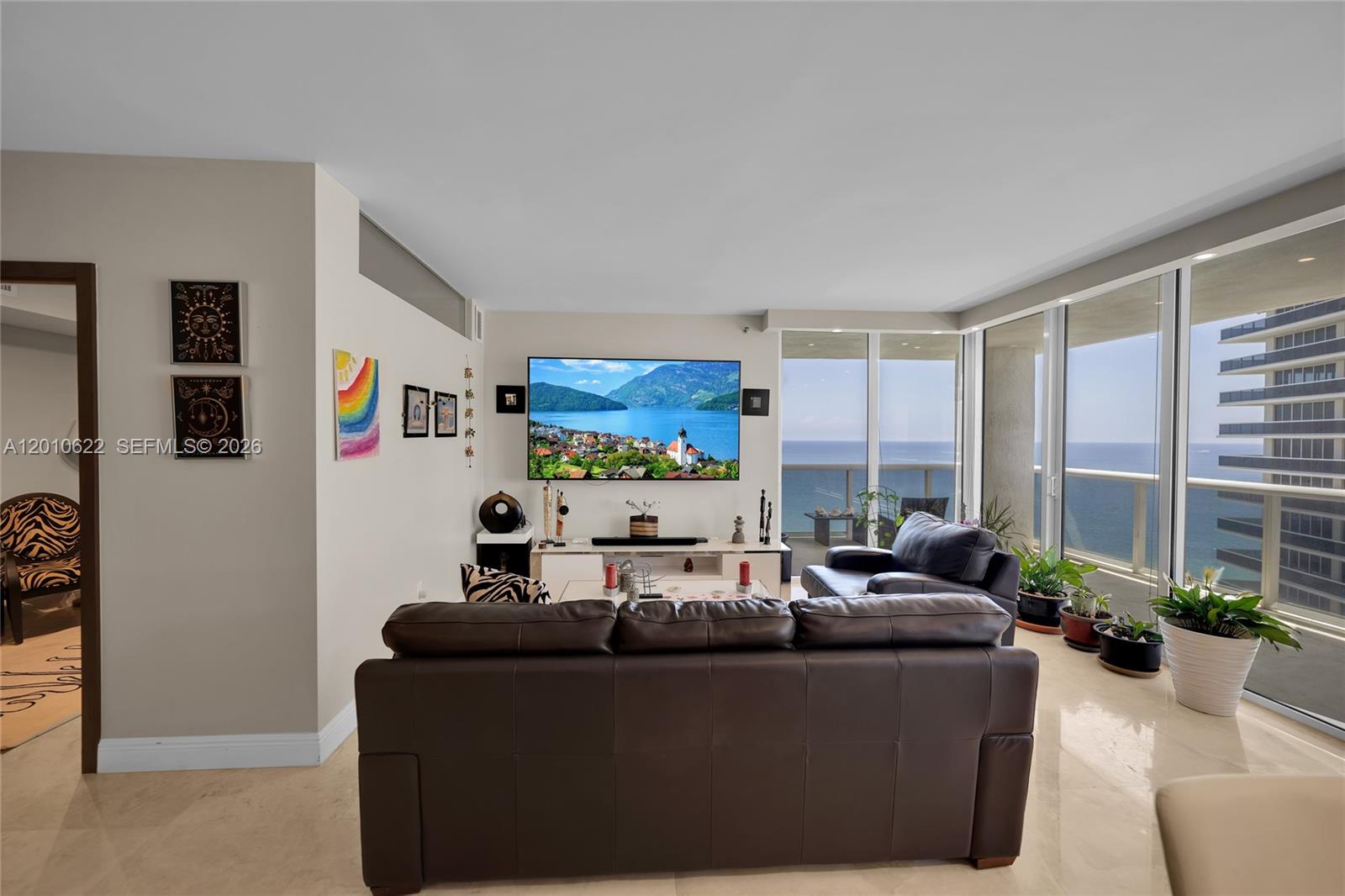 A living room features a dark leather sofa, a wall-mounted television, and floor-to-ceiling windows — 1800 S Ocean Dr # 2205, Hallandale Beach FL 33009, HALLANDALE BEACH, FL