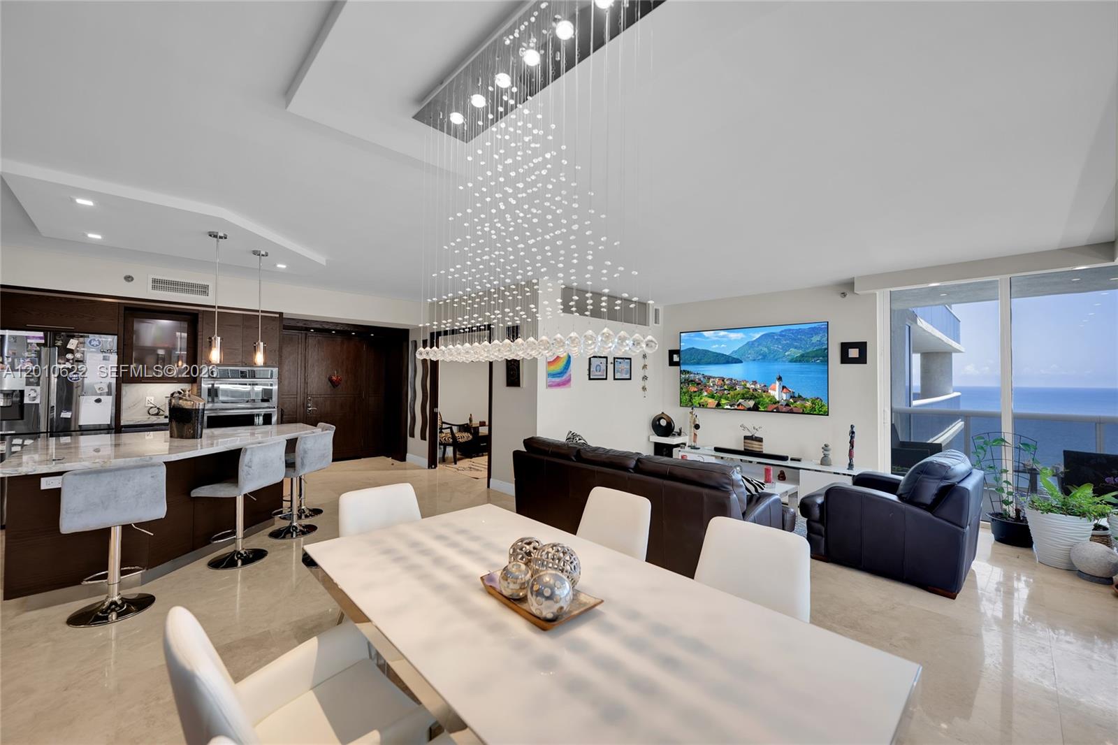 An open-concept living and dining area features a modern chandelier, kitchen island, and ocean view — 1800 S Ocean Dr # 2205, Hallandale Beach FL 33009, HALLANDALE BEACH, FL