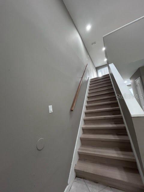 A staircase with light wood treads and a wooden handrail ascends against a gray wall — 4010 DOLOMITE STREET UNIT A6, ORLANDO, FL