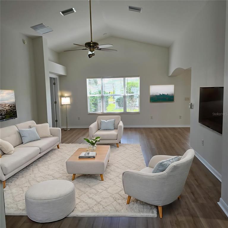 A living room with light-colored furniture, a white rug, and wood-look flooring under a vaulted ceiling — 1417 VALPARAISO STREET, THE VILLAGES, FL