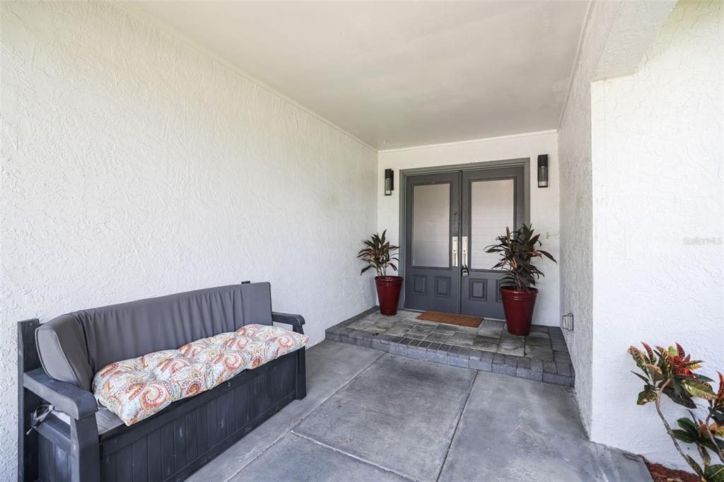 A covered entryway features a dark bench, two potted plants, and double glass doors — 10559 41ST COURT N, CLEARWATER, FL