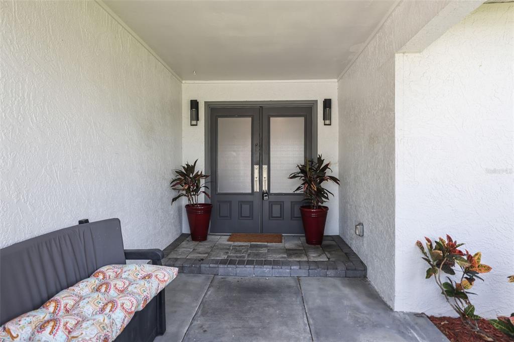 A covered entryway features a gray double door, two potted plants, and a patio bench — 10559 41ST COURT N, CLEARWATER, FL