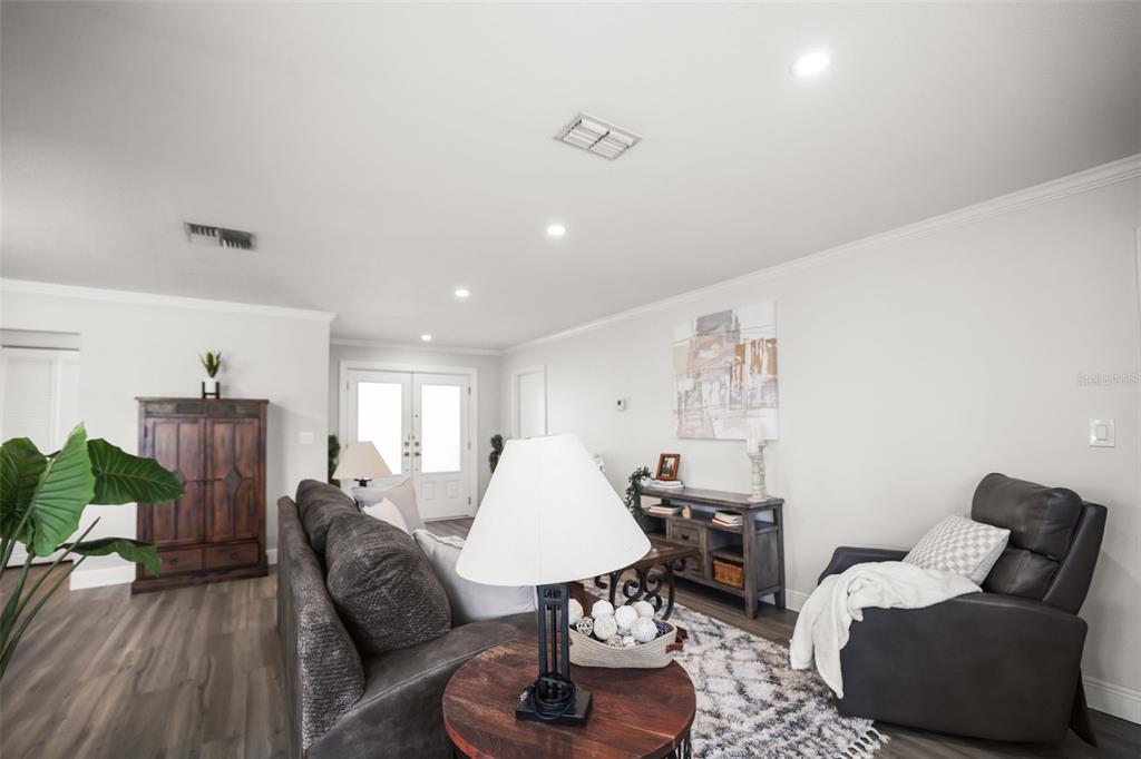 A living room features gray wood-look flooring, a dark sofa, a recliner, and white walls — 10559 41ST COURT N, CLEARWATER, FL