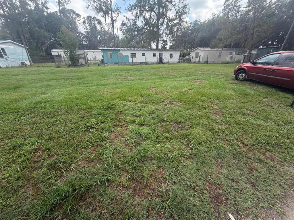 A grassy yard features a red car parked on the right and mobile homes nearby — 0 SUNSET CIRCLE, LAKE ALFRED, FL