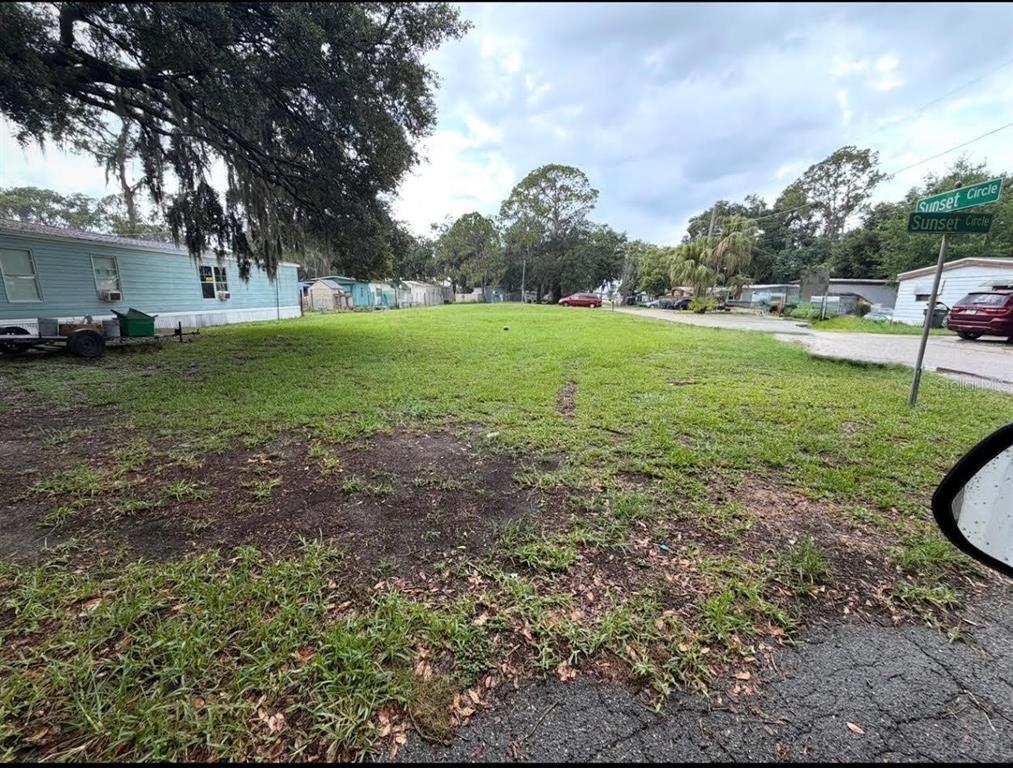 A grassy vacant lot sits next to a light blue mobile home on a street — 0 SUNSET CIRCLE, LAKE ALFRED, FL