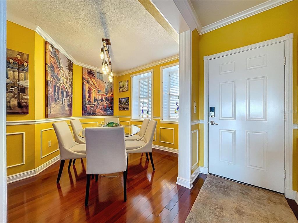 A dining room with yellow walls, wainscoting, hardwood floors, and a glass-topped table — 1200 COUNTRY CLUB DR UNIT 5404, LARGO, FL