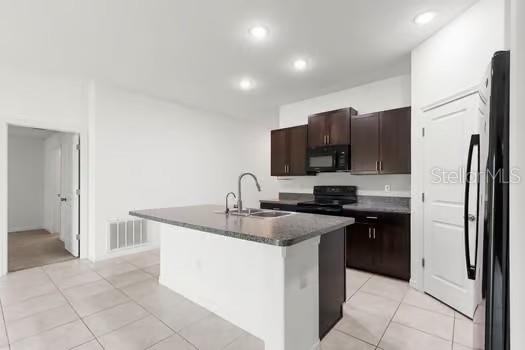 A kitchen features dark wood cabinets, a granite-topped island, and light tile flooring — 11207 SAGE CANYON DRIVE, RIVERVIEW, FL