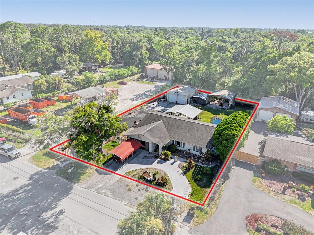 An aerial view shows a house with a red carport and several detached storage structures — 7813 LEO KIDD AVENUE, PORT RICHEY, FL