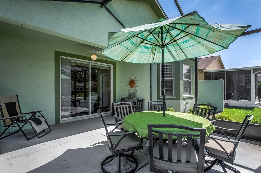 A covered patio features a dining set with a green umbrella and a sliding door — 20930 TANGOR ROAD, LAND O LAKES, FL