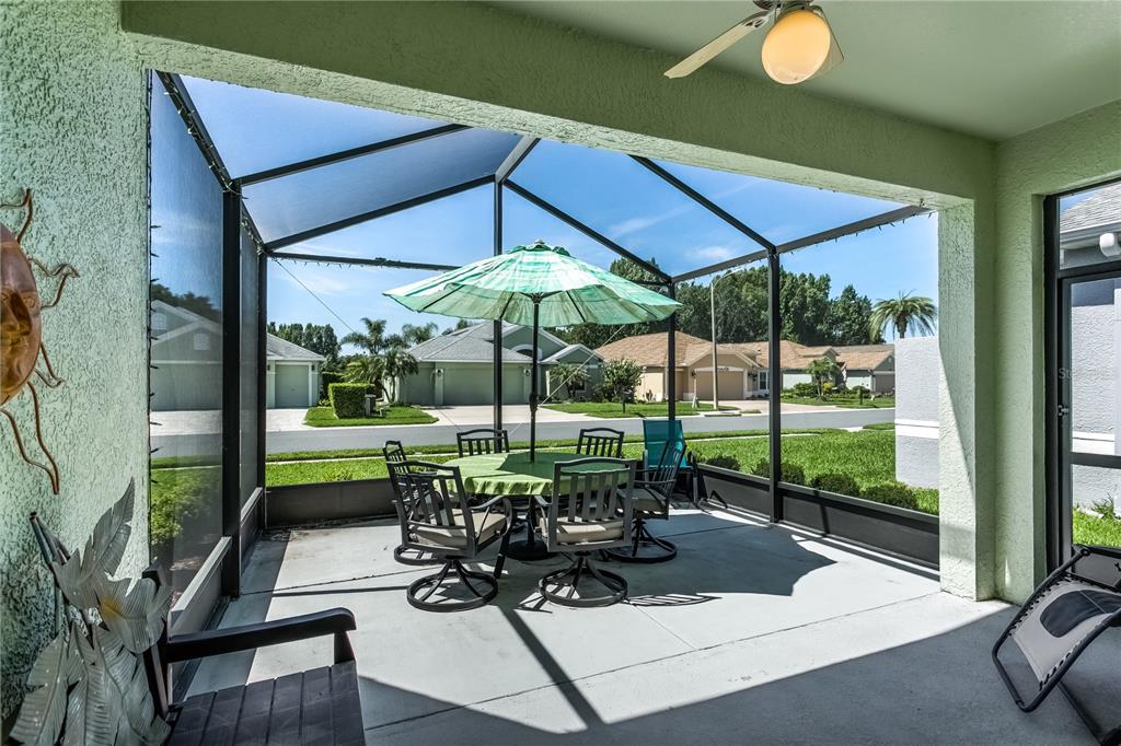 A screened-in patio features a dining set with a green umbrella and a ceiling fan — 20930 TANGOR ROAD, LAND O LAKES, FL