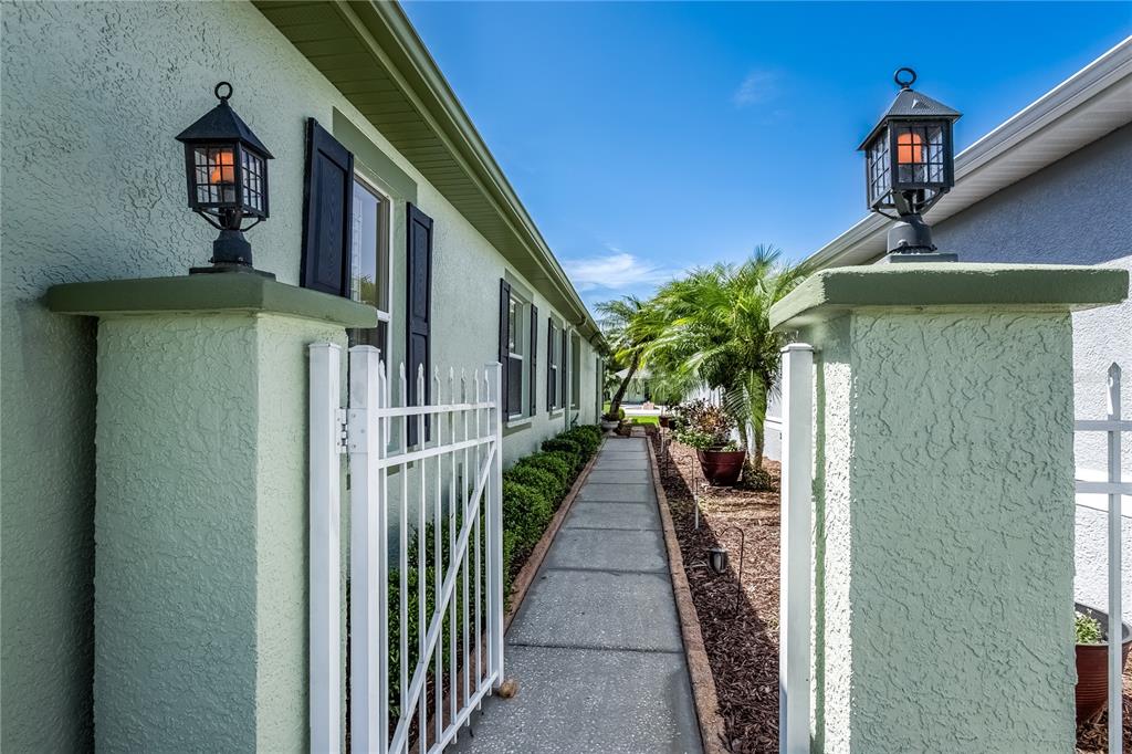 A concrete walkway leads between two stucco walls topped with outdoor lanterns toward a garden — 20930 TANGOR ROAD, LAND O LAKES, FL