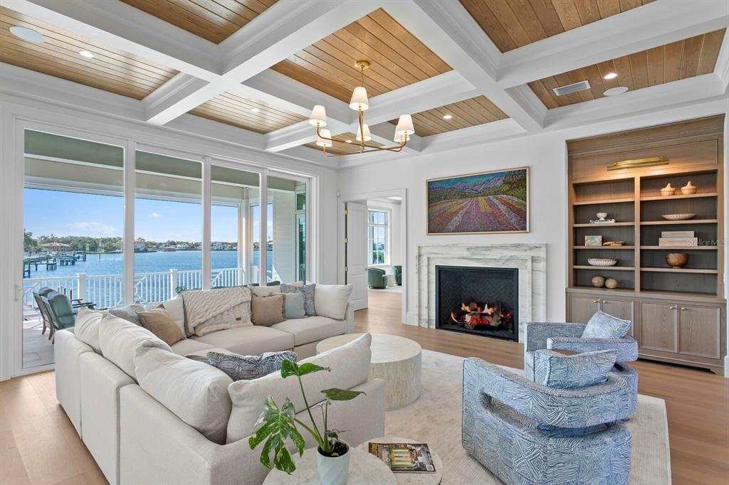 A living room features a coffered wood ceiling, fireplace, built-in shelving, and waterfront views — 16 SANDPIPER ROAD, TAMPA, FL