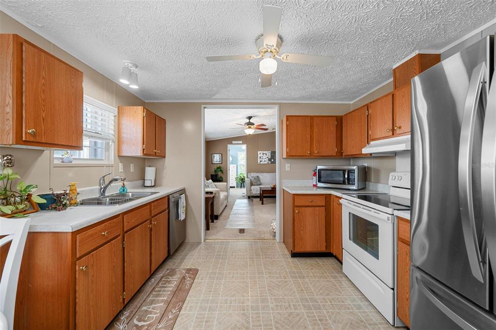 A kitchen with wood cabinets, white appliances, and a view into the adjacent living room — 1000 KINGS HIGHWAY UNIT 54, PUNTA GORDA, FL