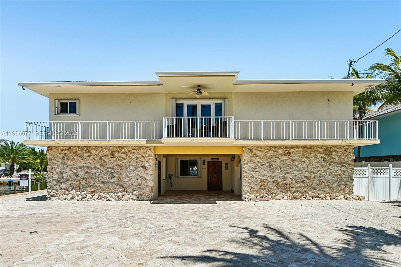 A two-story house features a stone-clad ground floor, a balcony, and a paved driveway — 201 Wildwood Cir, Key Largo FL 33037, KEY LARGO, FL