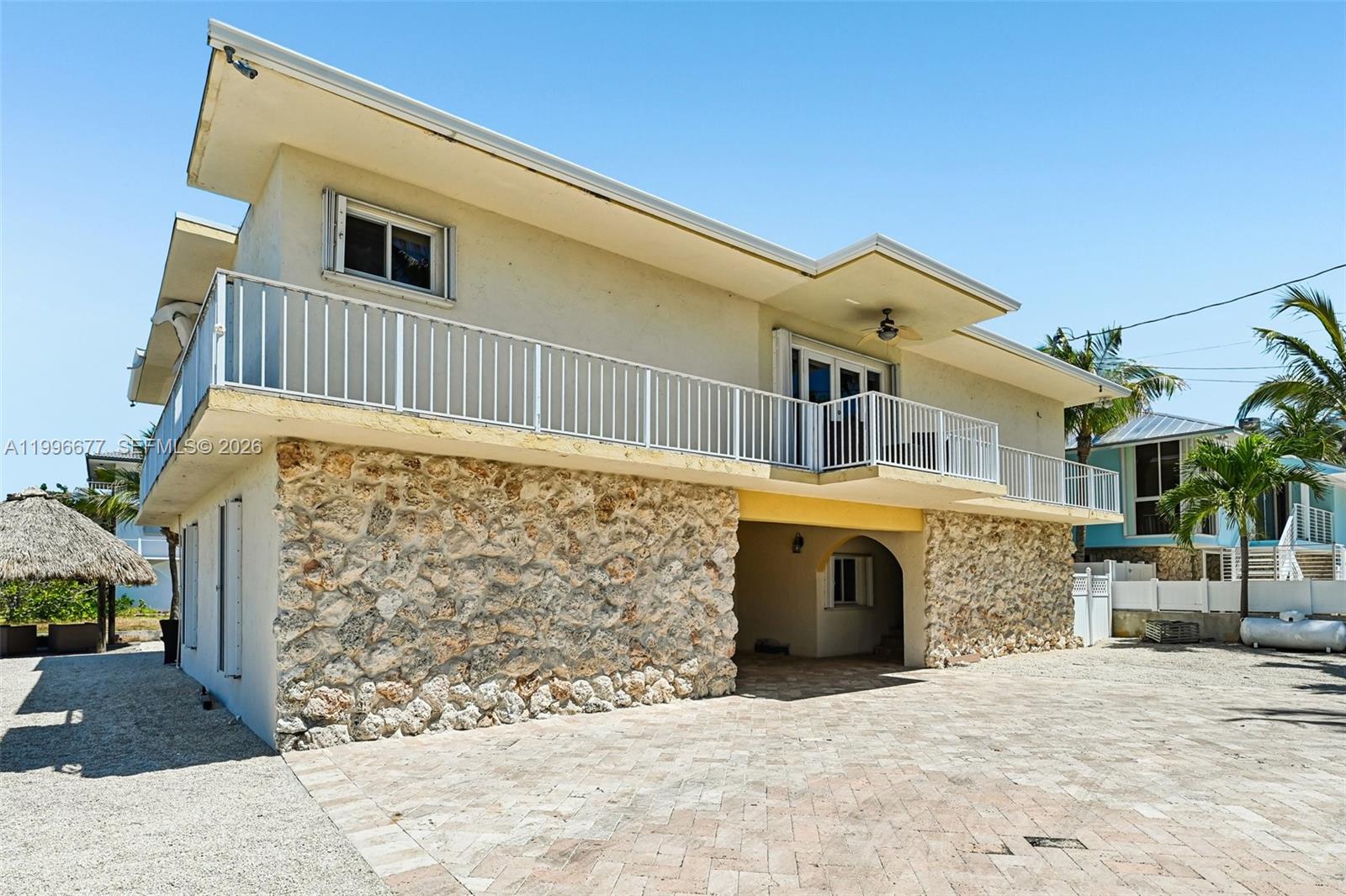 A two-story house features a stone-clad ground floor, a white balcony, and a paved driveway — 201 Wildwood Cir, Key Largo FL 33037, KEY LARGO, FL