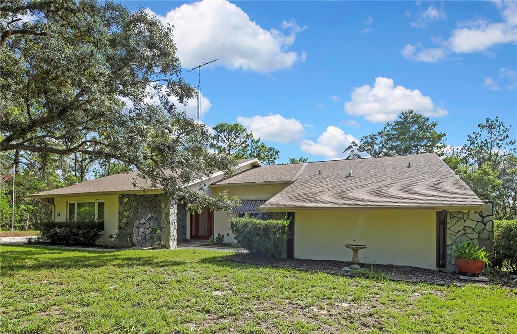 A single-story house with stone accents, a shingled roof, and a large tree in front — 12 MAYFLOWER COURT E, HOMOSASSA, FL